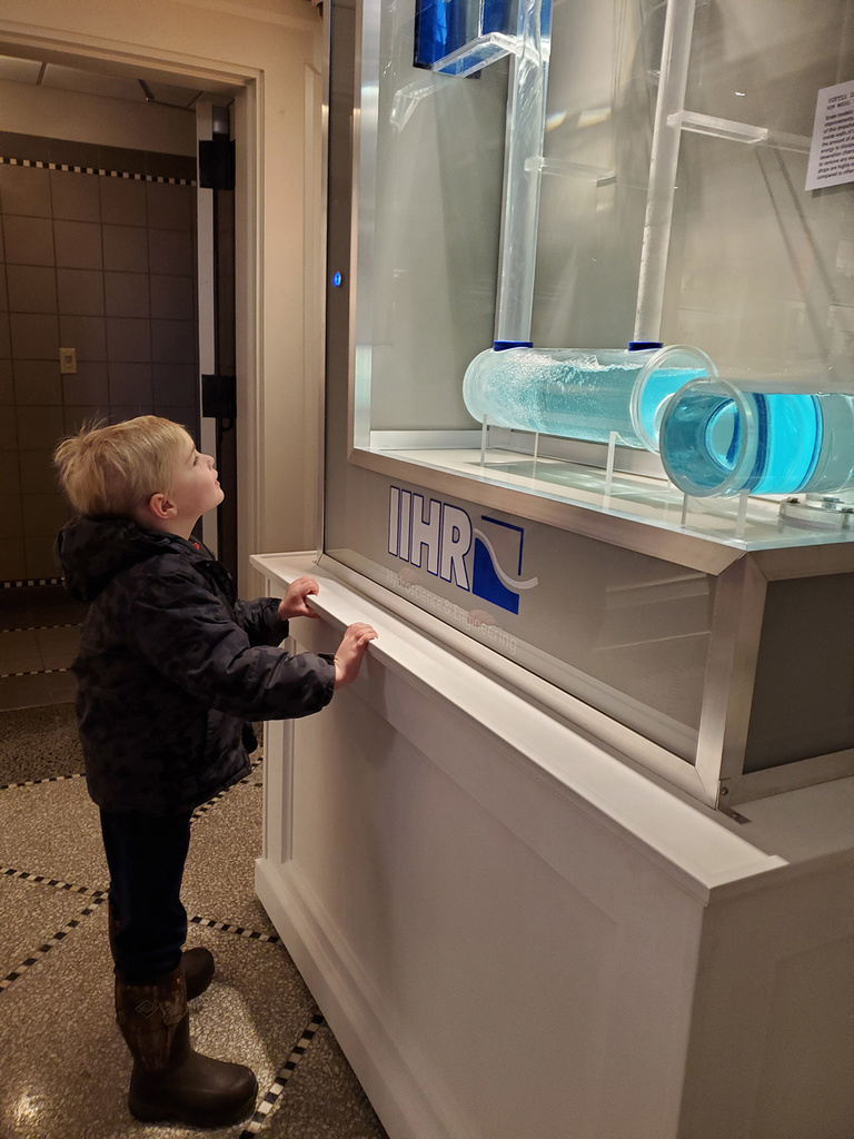 A little boy watches water flow through a mini-model of a dropshaft