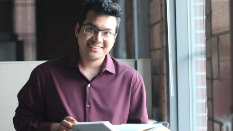 A young man smiles at the camera while holding a book